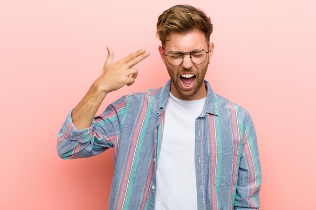 Young man looking unhappy and stressed, suicide gesture making gun sign with hand, pointing to head