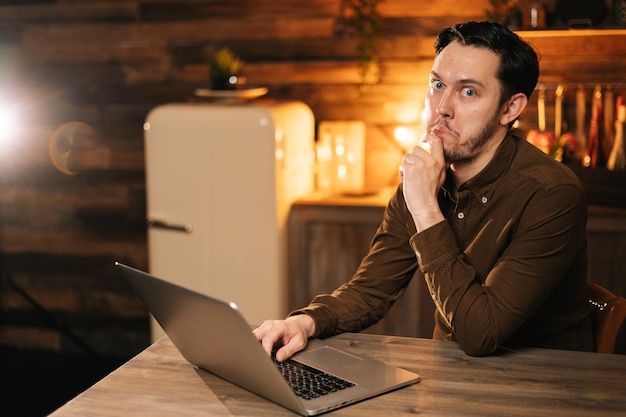 Young man looks into camera with shocked expression, freelancer working laptop at the home. Concept of lifestyle in self-isolation in Coronavirus COVID-19 Pandemic.