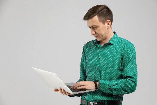 Young man looks at laptop screen in his hands and stands isolated 