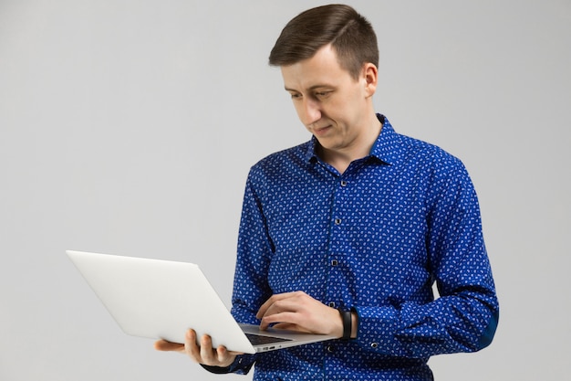 Young man looks at laptop screen in his hands and stands