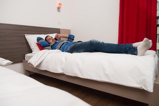 Young Man Lying On Bed And Having Fun On Phone In Bedroom