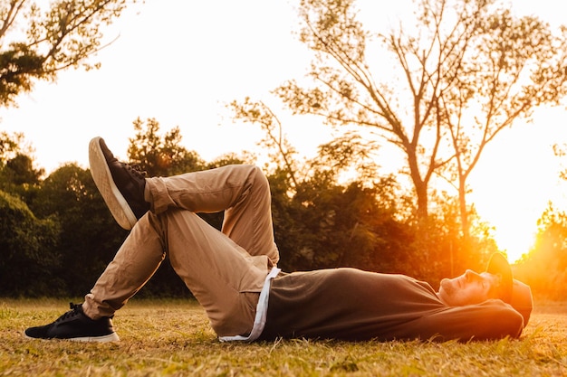 Фото Молодой человек, лежа на зеленой траве, наслаждаясь закатом релаксации в парке. понятие о свободе релаксации. место для текста или рекламы