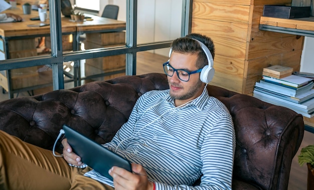 Young man lying on an office sofa with tablet