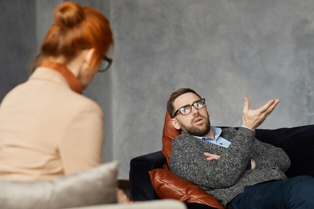 Foto giovane uomo sdraiato sul divano e parlando del suo problema allo psicologo durante la sua visita