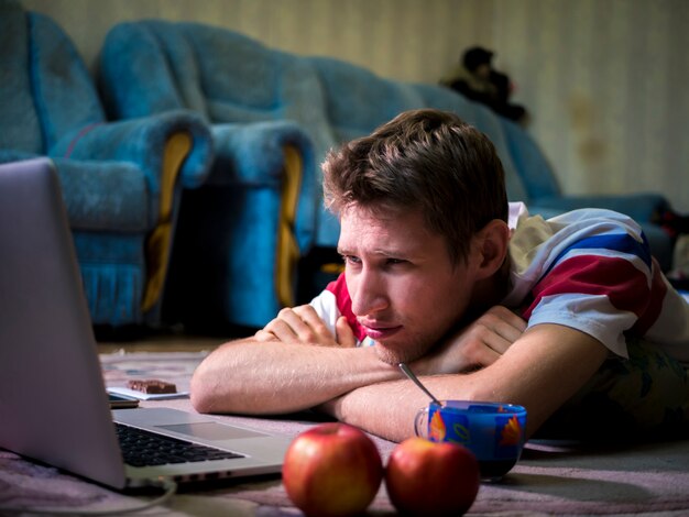 Young man lying and watching film using his laptop at home