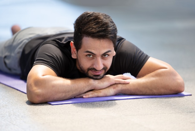 Young man lying on yoga mat and relaxing