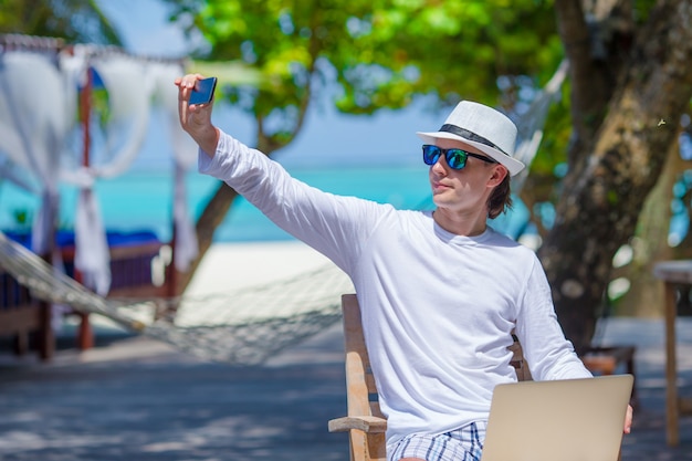 Young man make a photo on cell phone at tropical beach 