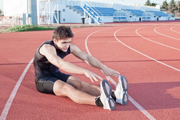 Un giovane fa un allungamento dell'atleta. sullo sfondo lo stadio.