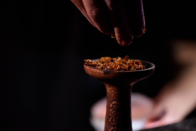 Young man makes hookah. Barman fills black burnt ceramic bowl for hookah smoking different types of tobacco.