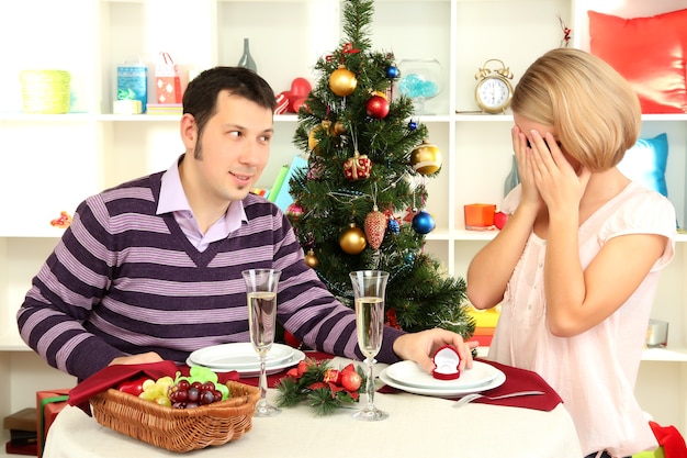 Young man makes proposal to marry girl at table near Christmas tree