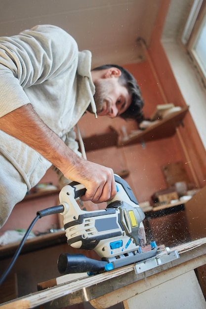 A young man makes repairs in the apartment. works with electric\
fretsaw is sawing plywood