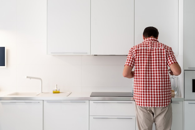 Young man makind tea standing next to the open fridge.