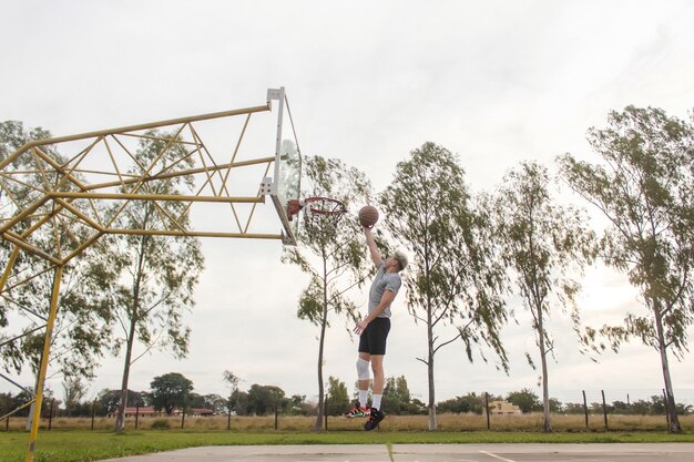 Young man making a jump shot to put the ball in the hoop on an abandoned court.