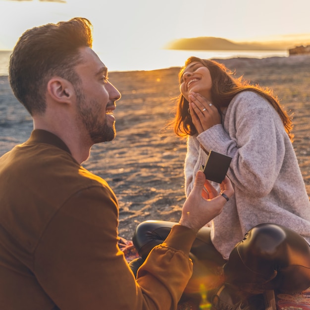 Foto giovane che fa proposta alla donna sulla riva di mare sabbiosa