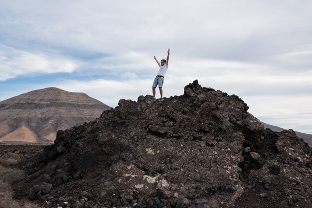 Young man making triumph gesture on top of a mountain.