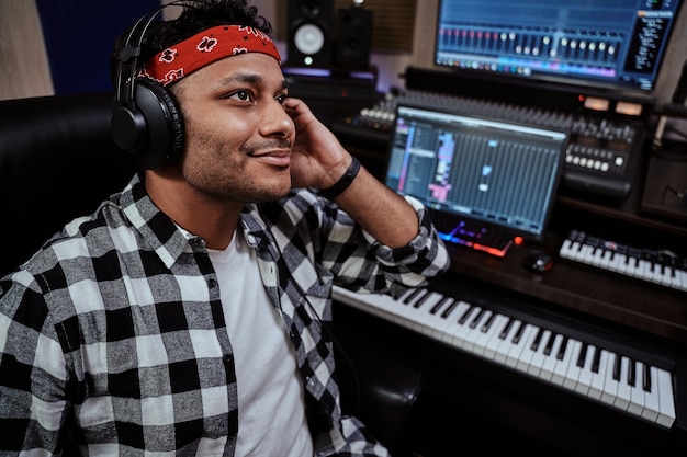 Young man male artist in headphones smiling while listening to music in recording studio