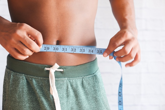 Young man measuring his waist with a tape measure, close up.