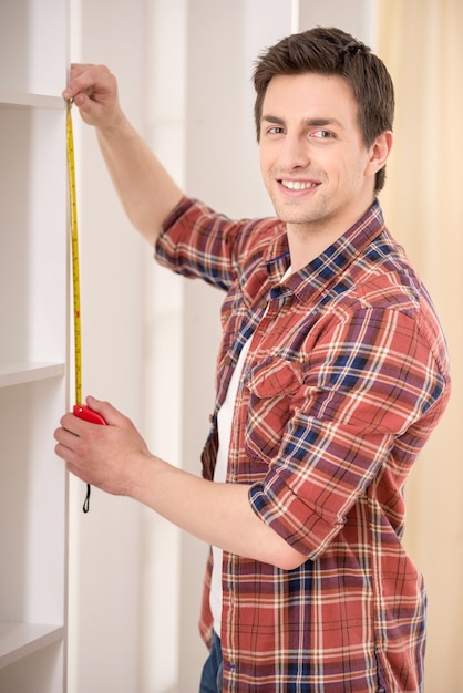 Young man measuring home furniture with measure tape.