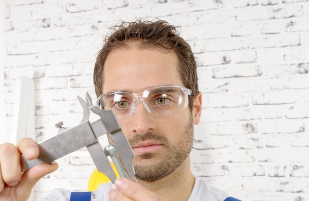 Young man measuring screw using caliper