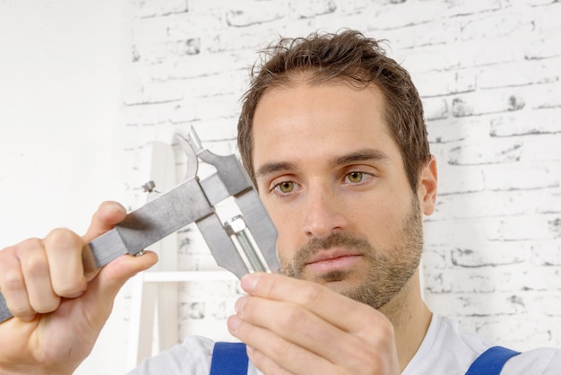 Young man measuring screw using caliper