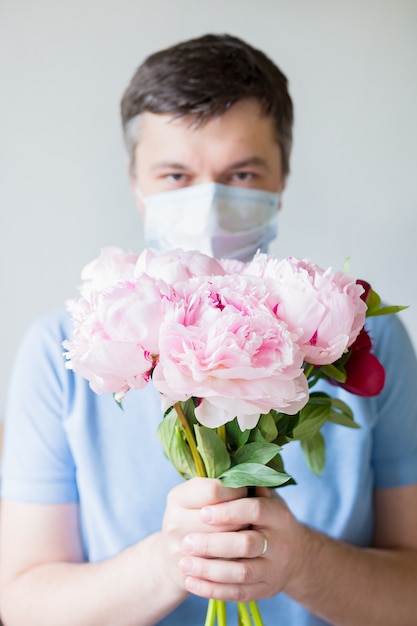 Foto giovane in fiori medici che tengono maschera. l'uomo in una maschera medica anti-virus detiene un mazzo di fiori. recupero da coronavirus. fermare la pandemia covid-19