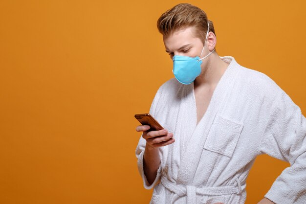 Young man in medical mask and housecoat in quarantine, social networks