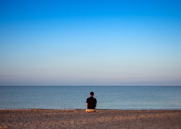 A young man meditates on the beach during sunset