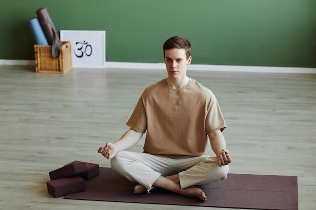 Young man meditating indoors sitting in lotus position