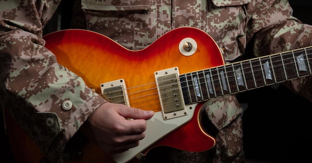 Photo young man in military uniform playing guitar close up view dark background