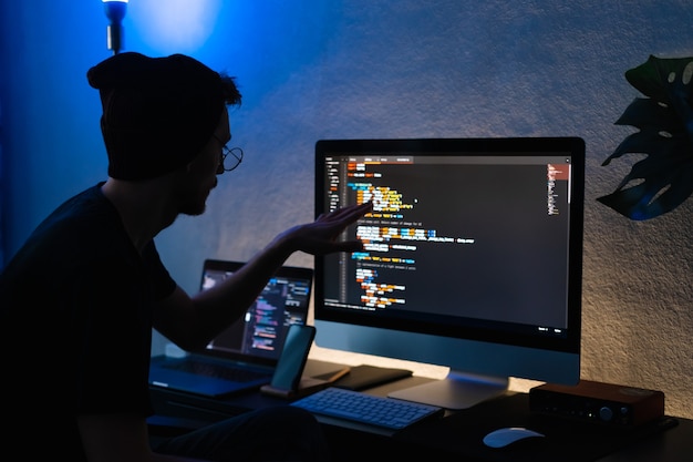 Young man mobile developer writes program code on a computer, programmer work in home office.