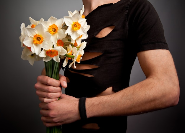 Young man in modern black clothing holding bouquet of narcissus flowers