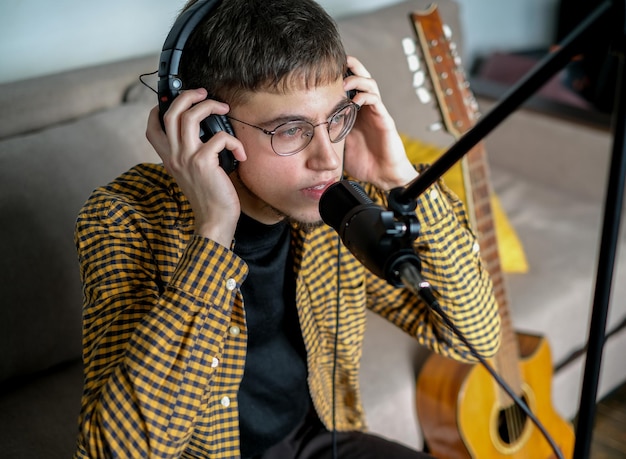 Foto giovane musicista che canta una canzone suonando la chitarra classica in uno studio musicale maschio che indossa le cuffie