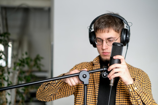 音楽スタジオでクラシックギターを弾いて歌を歌う若いミュージシャンイヤホンをかぶった男性