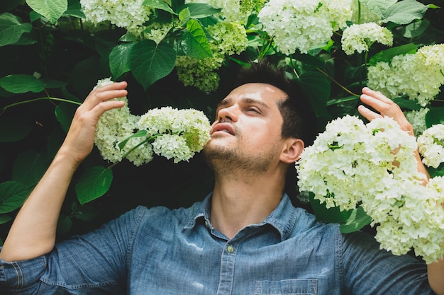 Young man near bush of white flowers in a garden