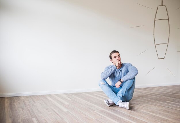 Photo young man in new home sitting on floor thinking about interior decoration