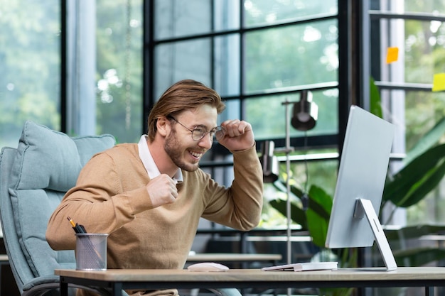 Young man in office celebrating victory and successful achievement results businessman holding hands