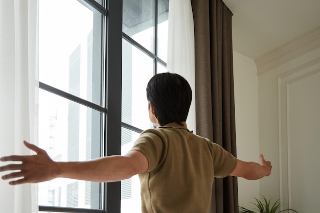 Photo young man opening curtains