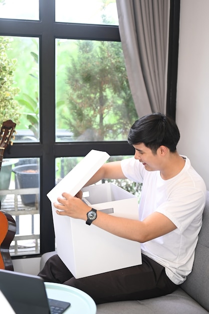 Young man opening gift box on sofa at home.