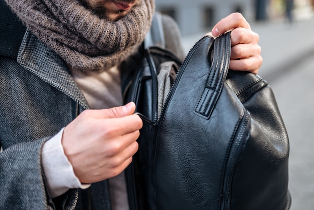 Young man opening his leather backpack.