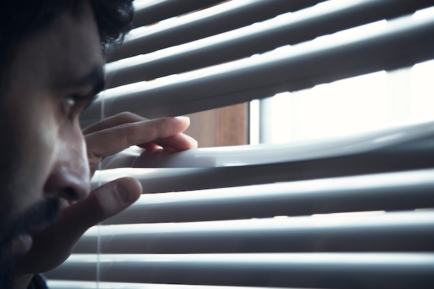 Young man opening window white blinds