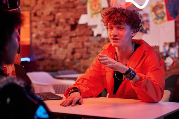 Young man in orange jacket looking at his girlfriend during conversation