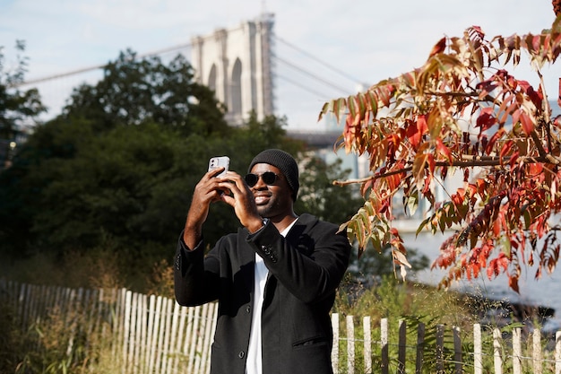 Photo young man outdoors exploring the city by himself and taking pictures with smartphone