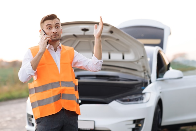 車の外の若い男。電話で話している失望した実業家