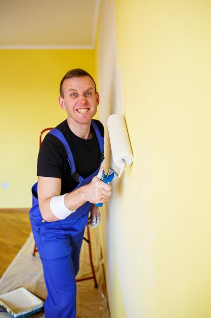 Young man in overalls hold a paint roller. tools accessories\
for apartment room renovation. home renovation concept