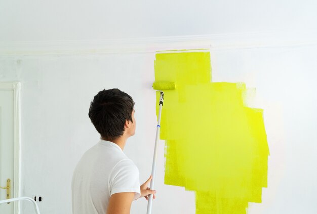 Young man painting wall in illuminating yellow color in the white plastered room