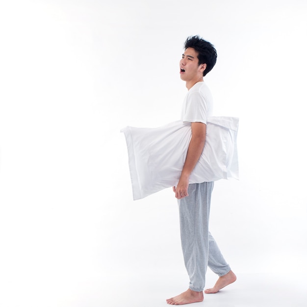 Young man in pajamas embracing white pillow isolated