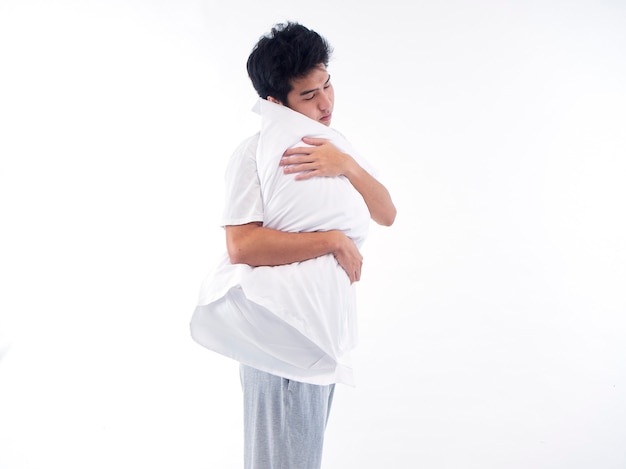 Young man in pajamas embracing white pillow isolated