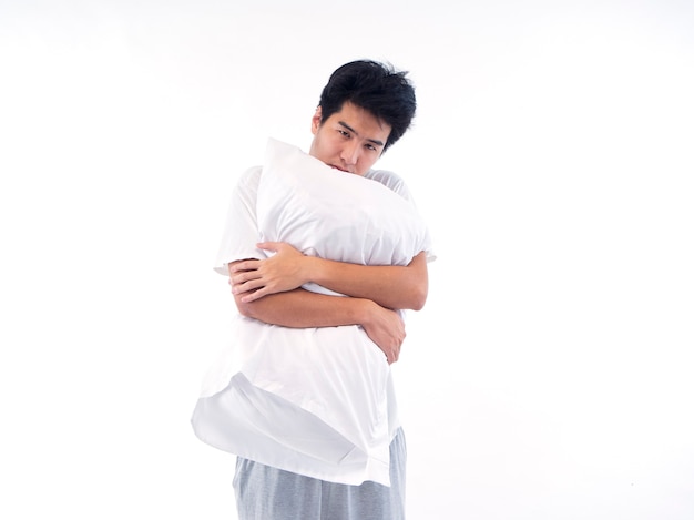 Young man in pajamas embracing white pillow isolated