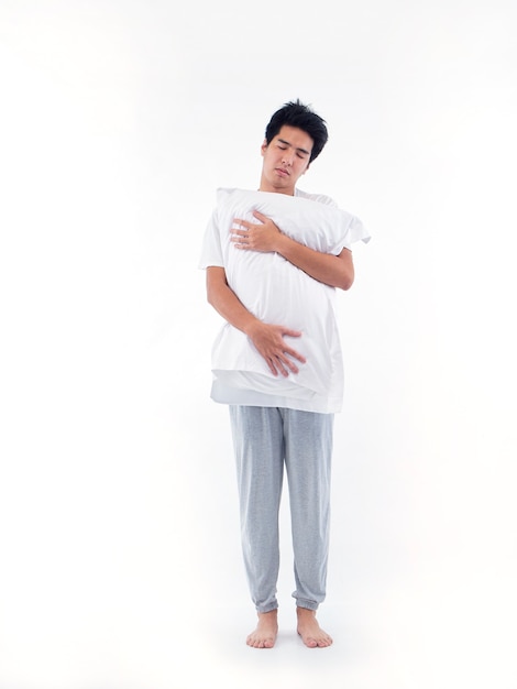 Young man in pajamas embracing white pillow isolated