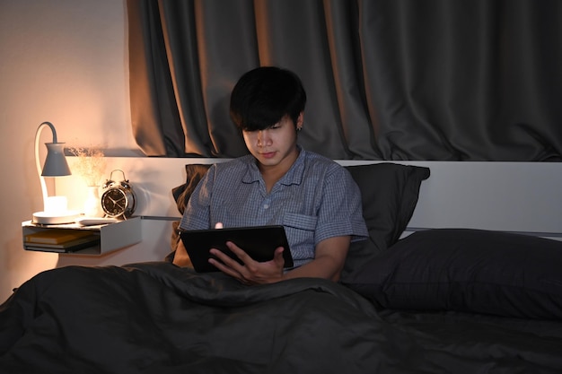 Young man in pajamas using digital tablet on his bed